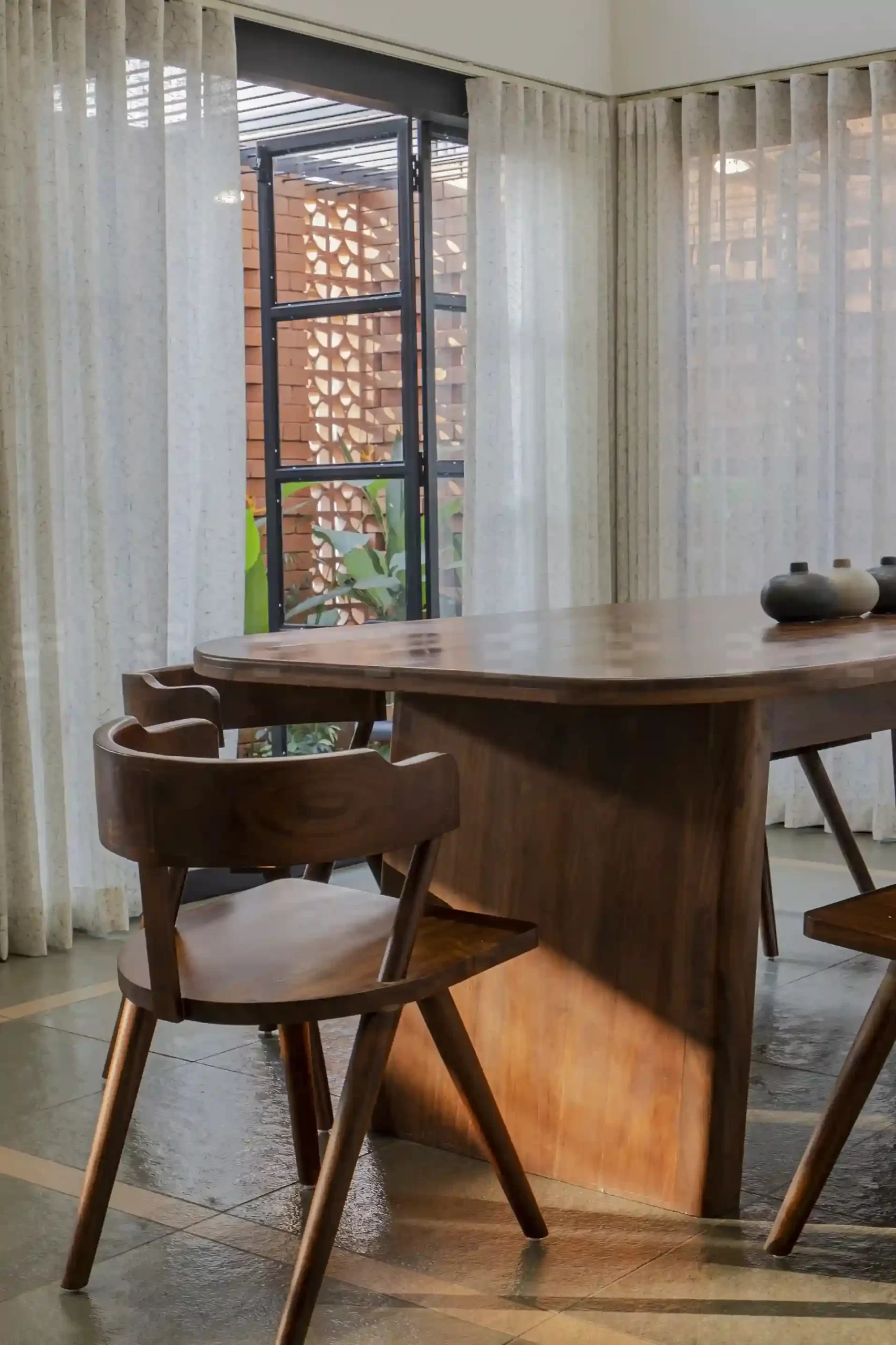 Modern dining area connected to a lush courtyard through wide glass doors, blending indoor and outdoor living in a Malappuram residence.