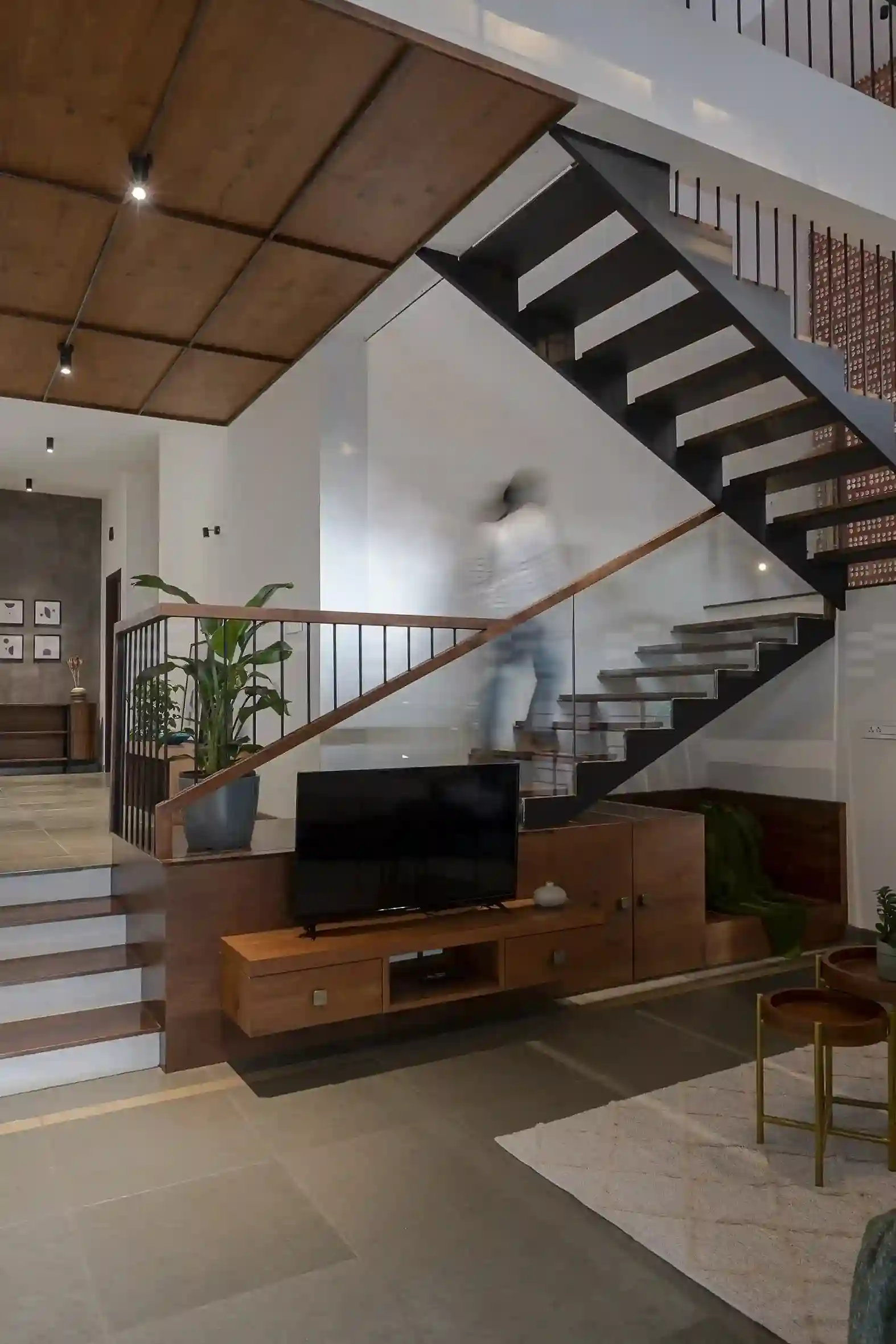 Contemporary staircase with wooden accents and glass railing connecting the living area to the dining space in a Malappuram residence.