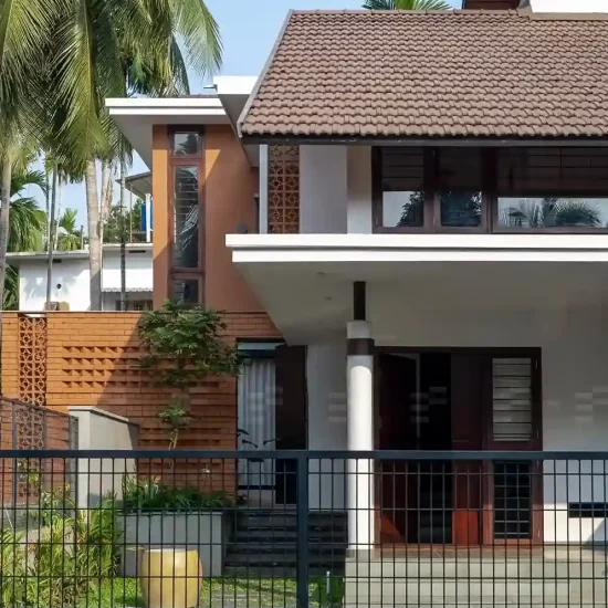 Modern Kerala home exterior designed by the top residential architects in Malappuram, featuring terracotta brick details, tiled sloped roof, and lush landscaping.
