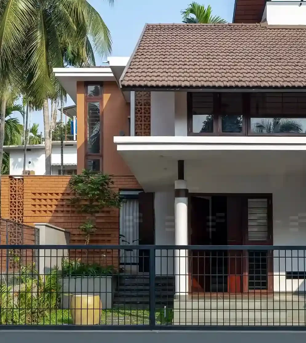 Modern Kerala home exterior designed by the top residential architects in Malappuram, featuring terracotta brick details, tiled sloped roof, and lush landscaping.