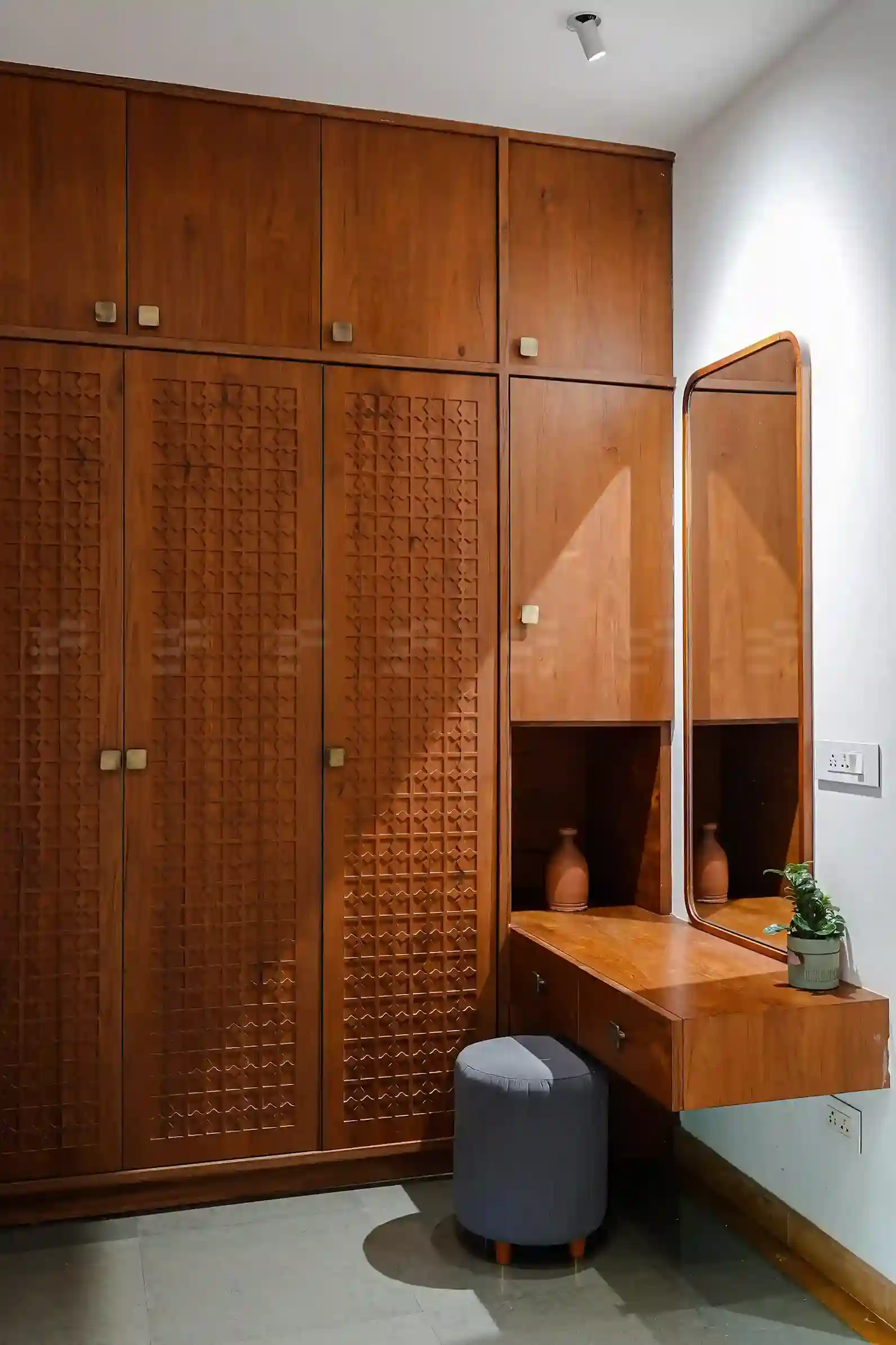 Custom wooden wardrobe with intricate carved panels and built-in dressing table in a modern Malappuram home interior.