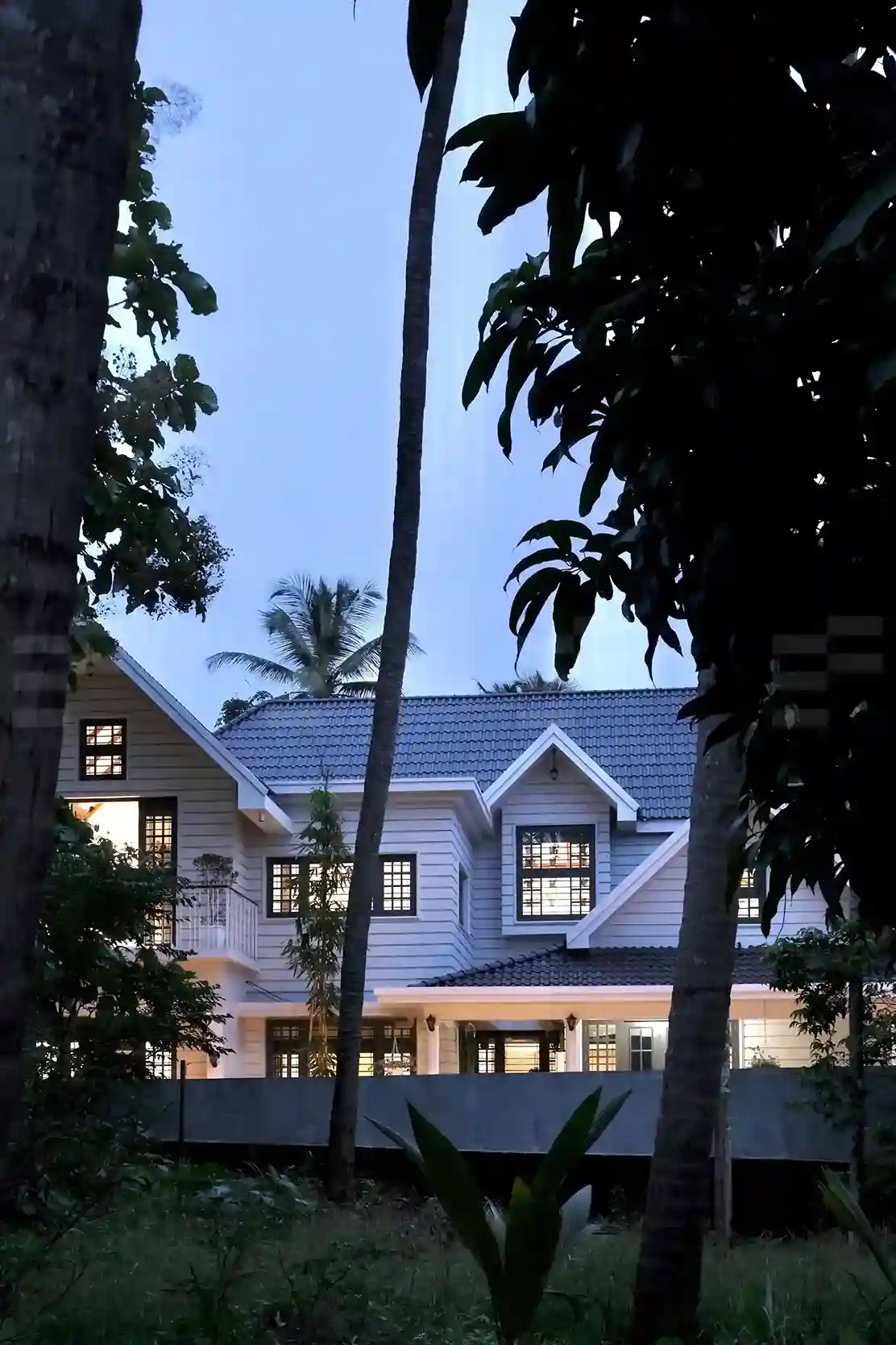 Front view of Kerala colonial house design at night, with warm lighting highlighting pillars, and arches.