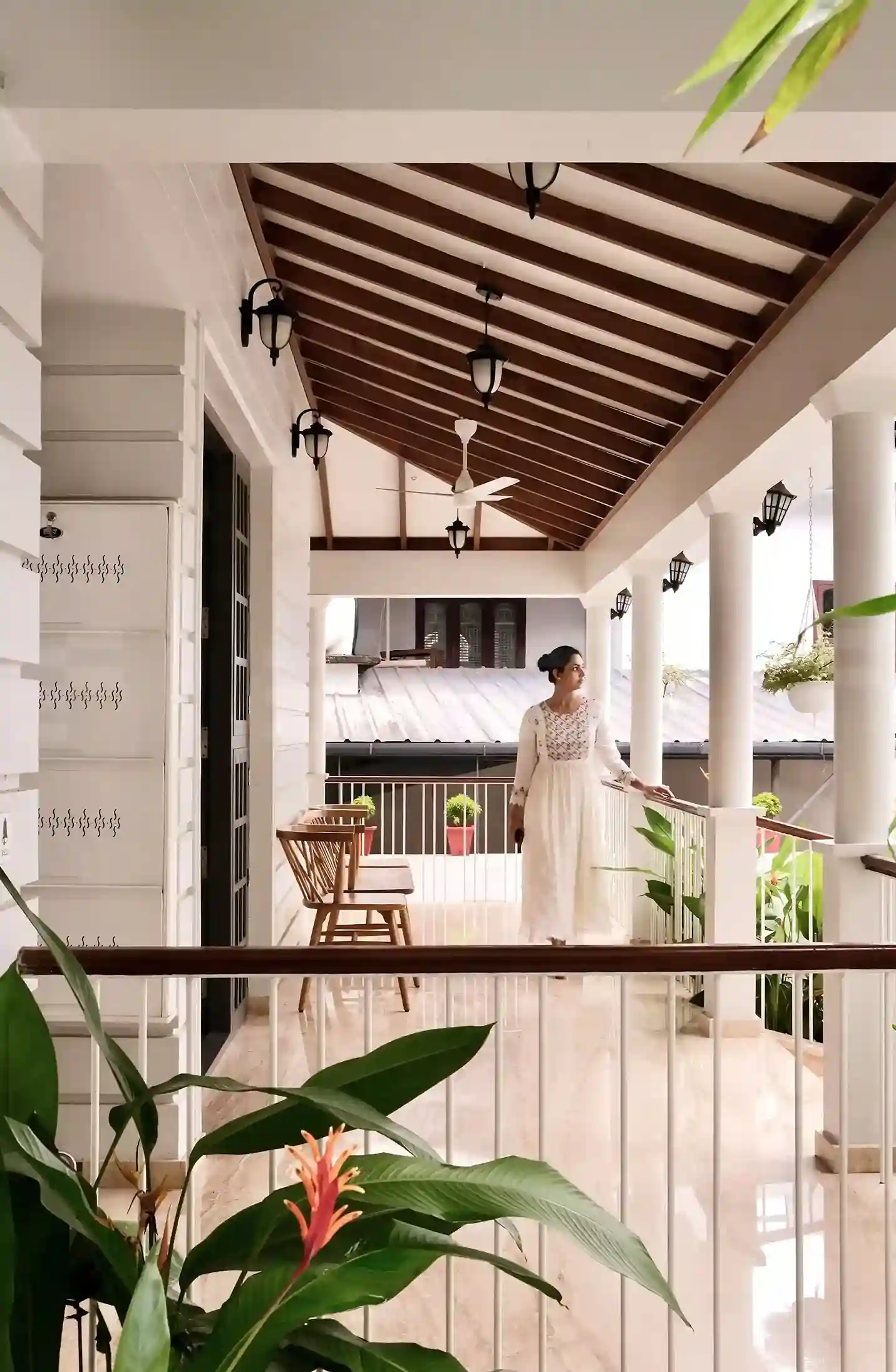 Elegant colonial style sit-out featuring white pillars, tiled flooring, and surrounding greenery for a calm and welcoming entrance.