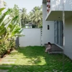 Contemporary house design Kerala – garden-side view with tropical plants and child near modern deck.