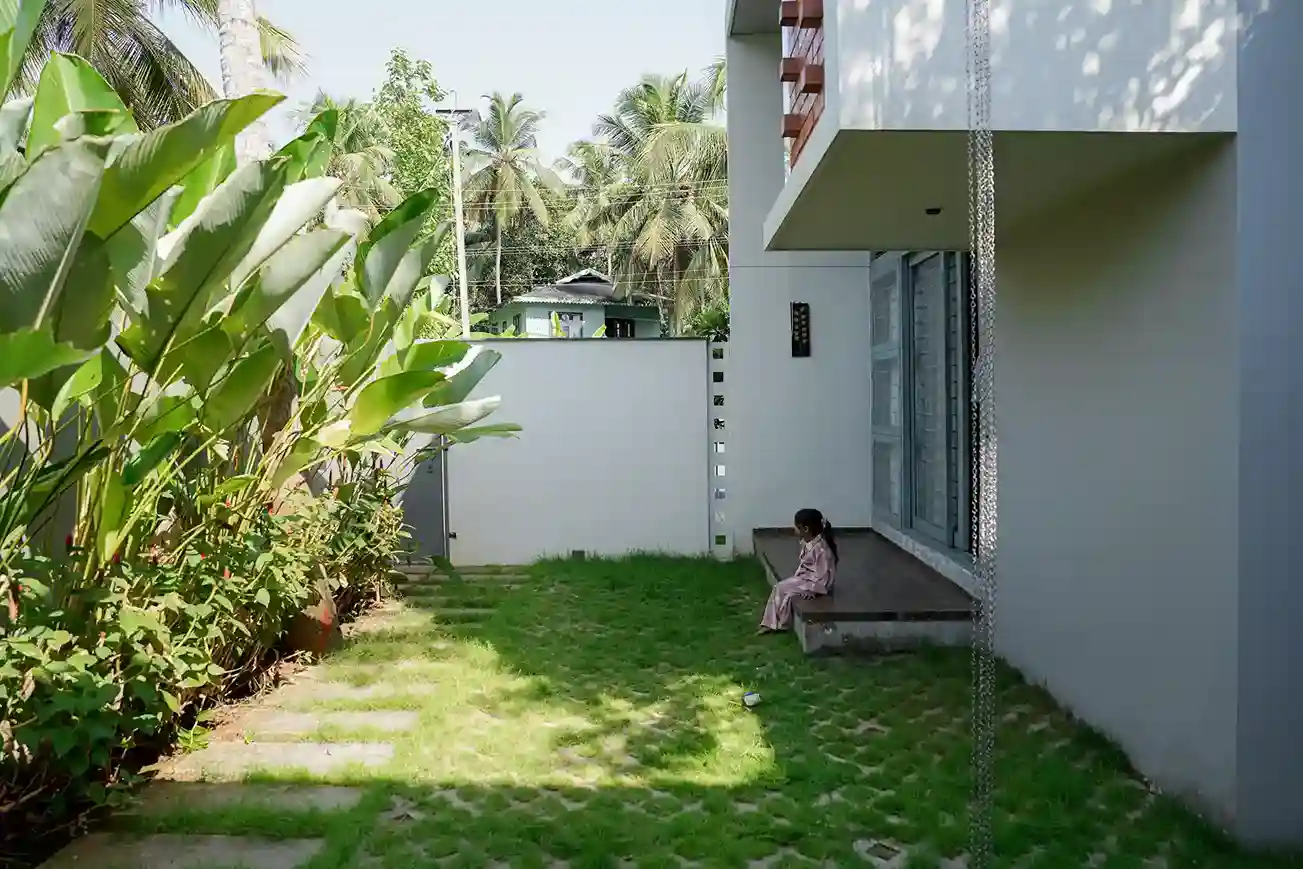 Contemporary house design Kerala – garden-side view with tropical plants and child near modern deck.