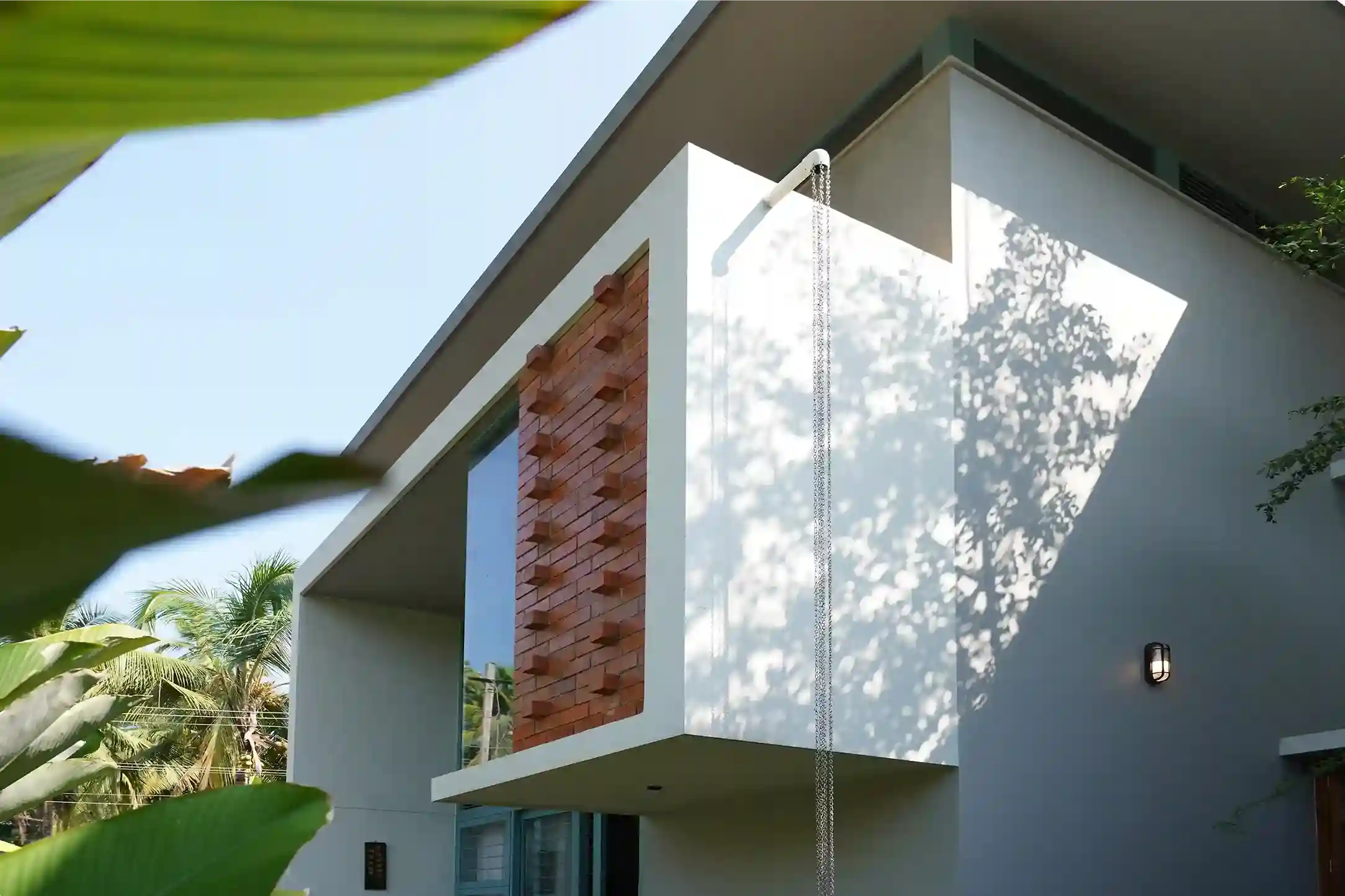 Contemporary house design Kerala – close-up of brick jaali, glass panel, and rain chain casting shadows.