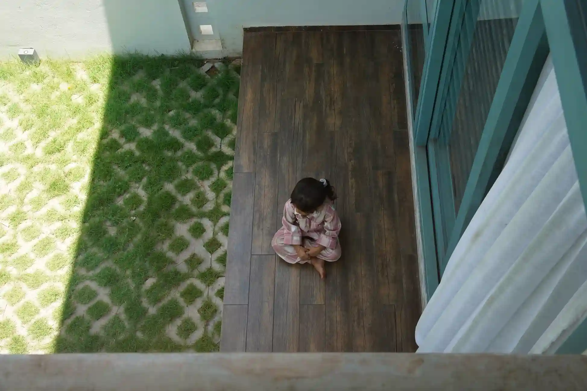 Contemporary house design Kerala – young girl on a wooden deck beside sliding windows with white curtains.