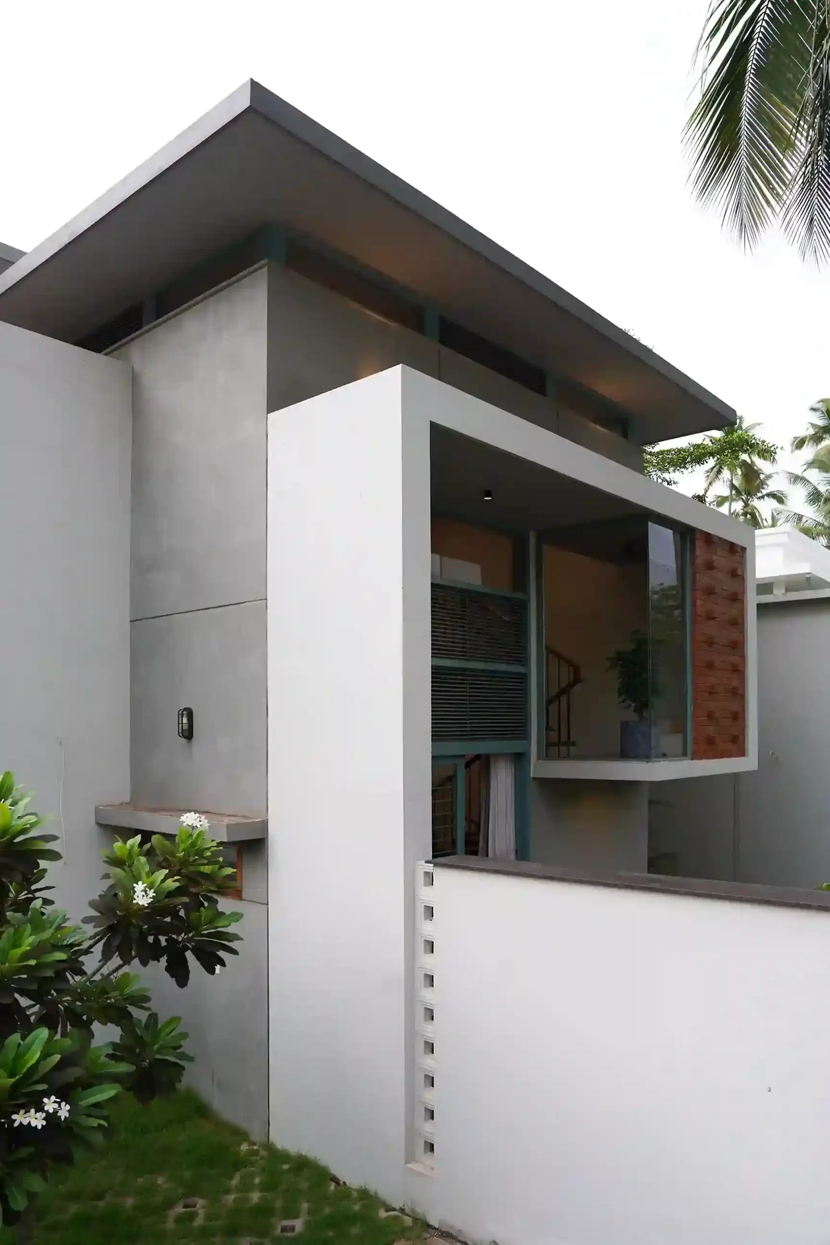 Contemporary house design Kerala with exposed brick, concrete textures, and large blue-grey framed windows – side facade view.