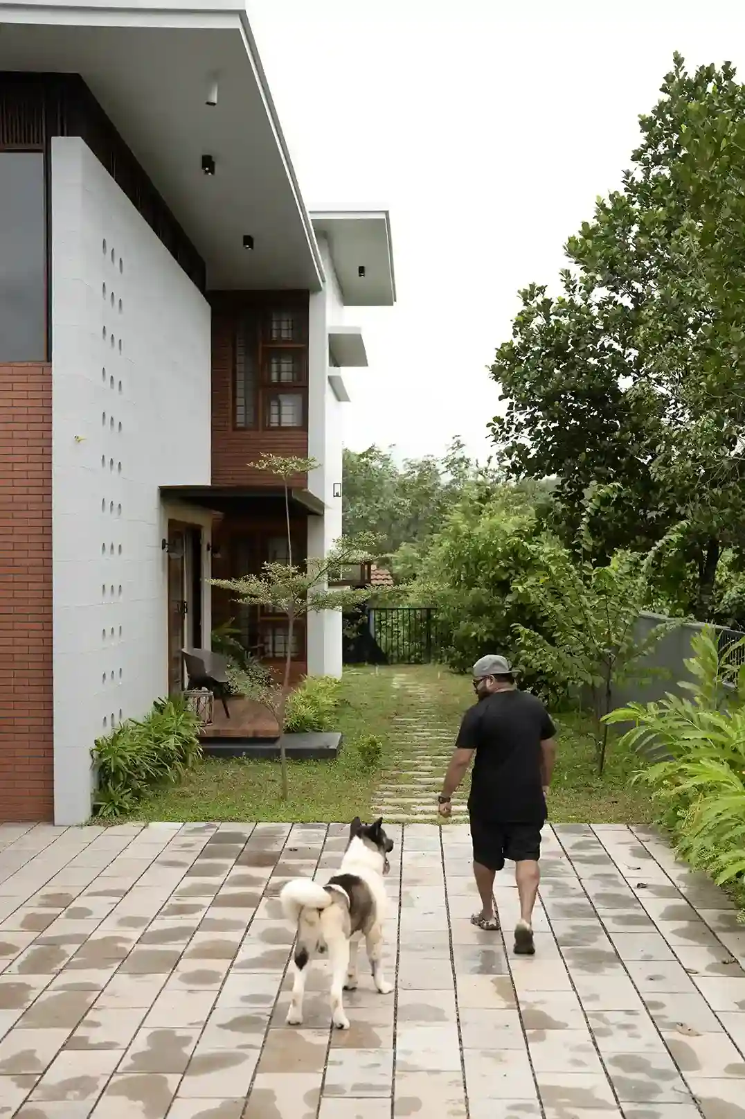 View of the paved front yard pathway and lush side garden leading to the entrance of the sustainable Kerala home.