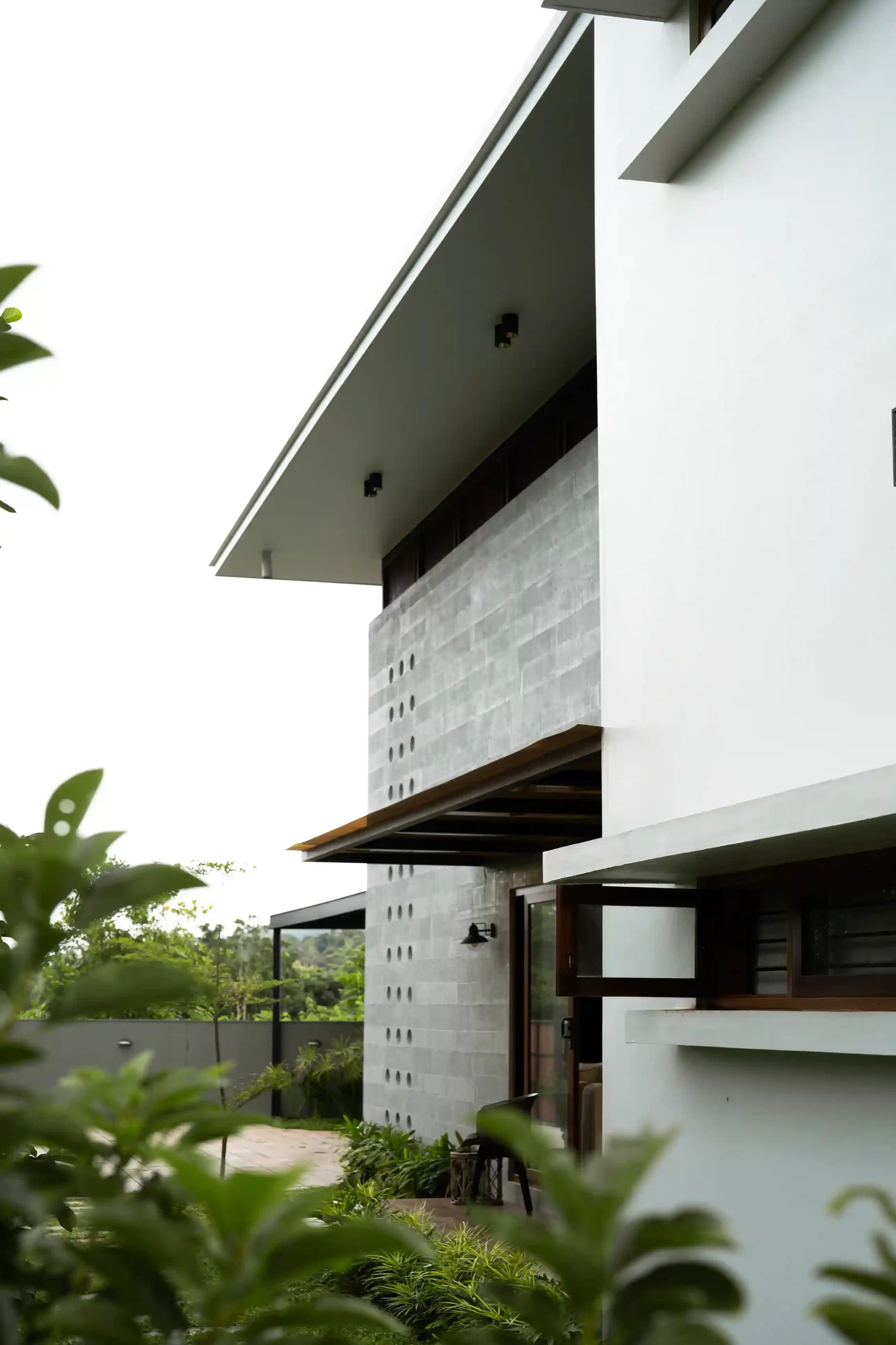 Close-up of the large cantilevered roof overhang and the decorative, light-filtering perforated gray wall element of the modern architecture.