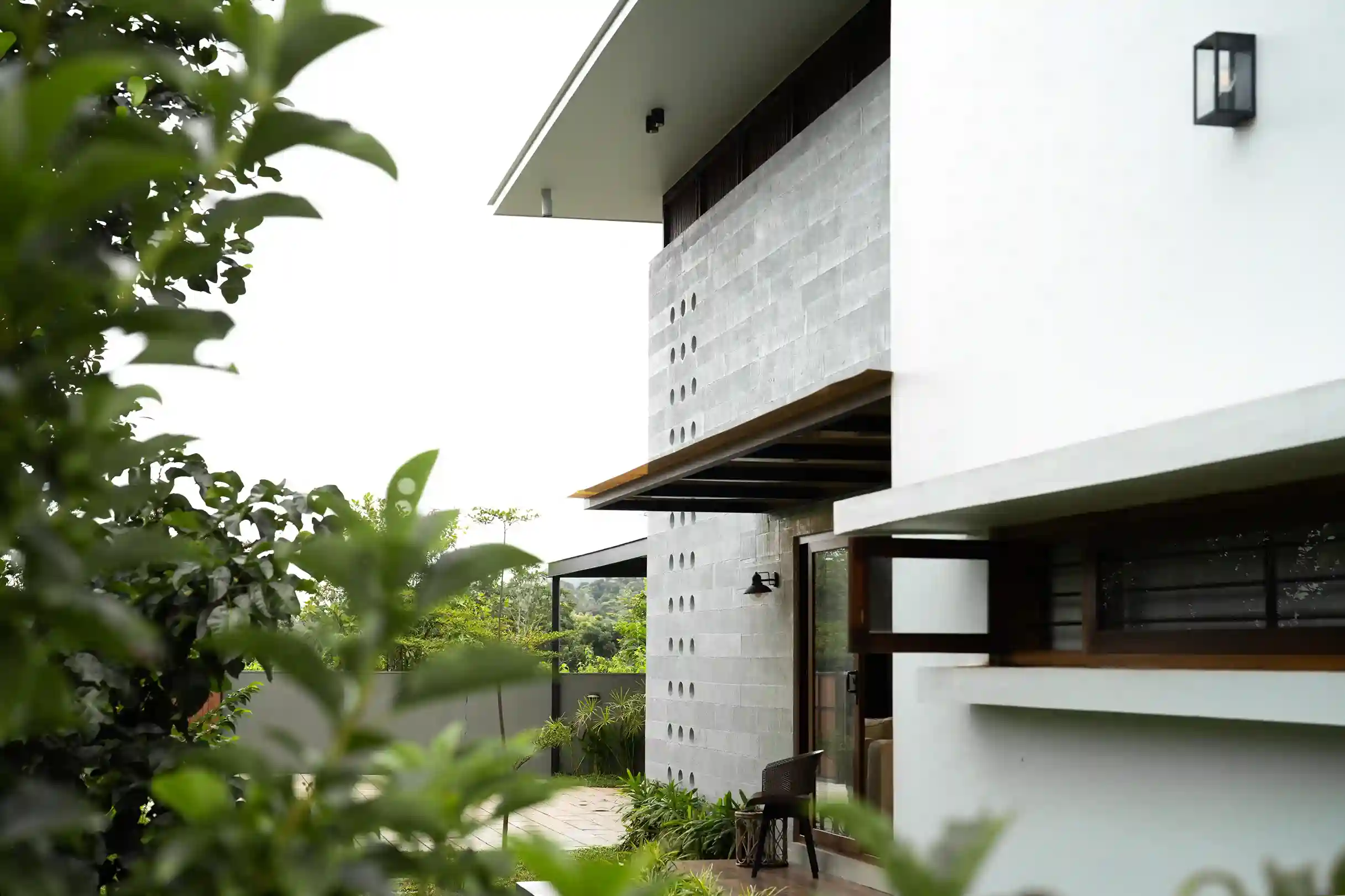 Detail of the Tropical Modern house side entrance with perforated gray block wall and lush green foreground.